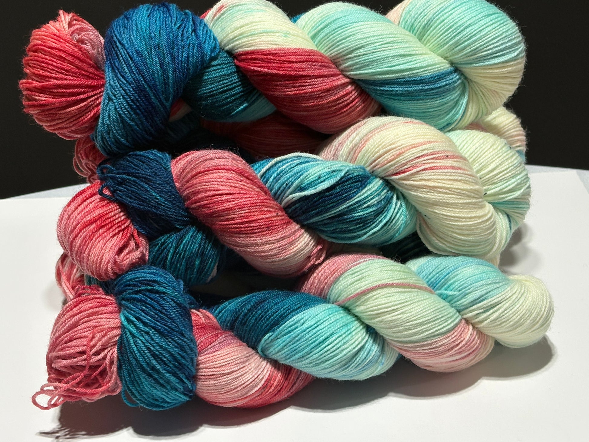 Hand-dyed fingering weight yarn sock set in patriotic red, white, and blue with a coordinating pale gray mini skein. The main skein features deep navy, aqua, creamy white, and vermilion sections with subtle charcoal speckles.