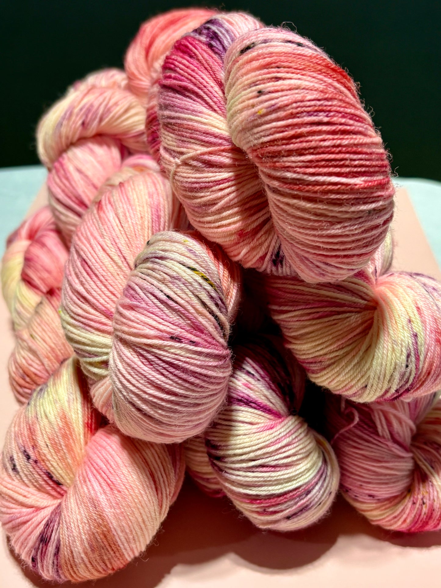 Hand-dyed fingering weight yarn in layered watercolor pinks with subtle olive and wine speckles inspired by pressed rose petals.